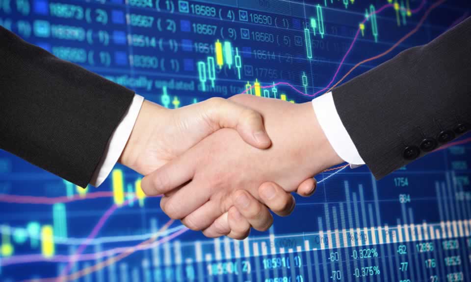 Two business men shake hands against a backdrop of charts and graphs
